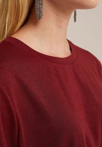 Burgundijas īsā piedurkne top ar apaļu kakla izgriezumu, ar teksturētu virsmu, kas zibenīgi atspoguļo gaismu. Zīda audums, gluda tekstūra.
