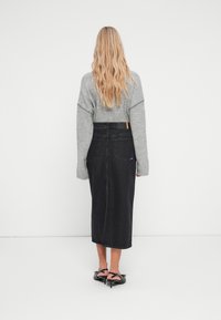 Črna denim midi krila z ravnim krojem, v kombinaciji s svetlo sivo pleteno jopico in črnimi čevlji s peto. Minimalistični dizajn.