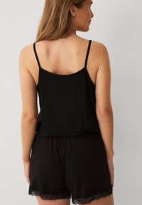 Zwarte camisole met dunne bandjes en een losse pasvorm, gecombineerd met zwarte shorts met kantafwerking. Zacht materiaal en eenvoudig ontwerp.