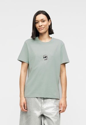 Svijetlozelena pamučna majica kratkih rukava s centralnim prikazom lika u sunčanim naočalama, naglašenim kružnim uzorkom od točkica.