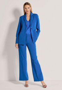 Felblau op maat gemaakt pak met een dubbel vest, wijde broeken en een top met v-hals; gladde stof en twee voorkruipl pockets.