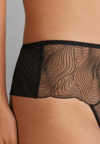 Black lingerie featuring a sheer mesh design with wavy patterns, outlined edges, and a smooth waistband, highlighting its texture and form.