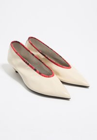 Zapatos de charol beige con punta afilada y un tacón bajo, con un forro rojo texturizado a lo largo de la abertura.
