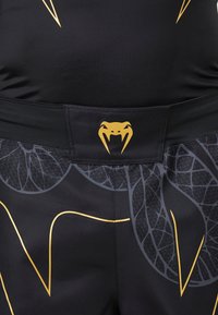 Schwarze Shorts mit grauen Blattadern und goldenen geometrischen Linien, die ein goldenes Schlangenkopf-Logo am Bund haben.