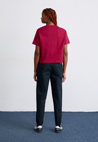 Bordeauxfarbenes kurzärmeliges Crop-Top kombiniert mit schwarzer, schmal geschnittener Hose und weißen Sneakers, das ein schlichtes Design und eine entspannte Passform zeigt.