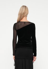 Black long-sleeve top with a velvet texture and sheer mesh panel. Features a rounded neckline and a fitted silhouette.