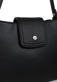 Czarna skórzana torebka charakteryzuje się teksturowaną powierzchnią, magnetycznym zapięciem oraz metalowym logo. Kompaktowy, prostokątny kształt z płaskim dnem.