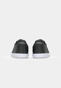 Fekete szintetikus sportcipők sima textúrával, fehér gumitalppal és hímzett logóval a saroknál; minimalista design.