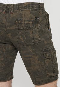 Cargo-Shorts aus einem dunkelgrünen strukturierten Stoff, mit einem Camouflage-Muster, einem elastischen Bund und mehreren Taschen mit Nähten.