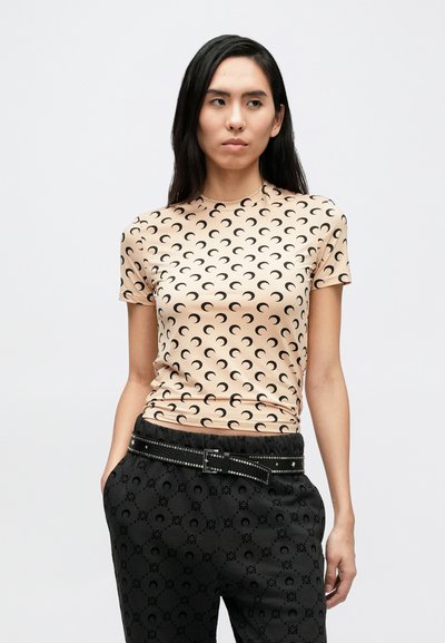 Világos őszibarackszínű rövid ujjú felső fekete félhold mintával, fekete nadrággal, díszes övvel.