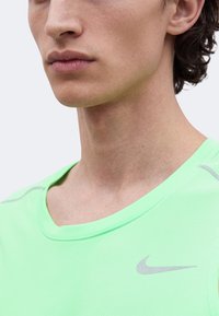Gros plan d'une personne portant un t-shirt de sport Nike vert clair avec un col rond et un logo visible sur la poitrine.