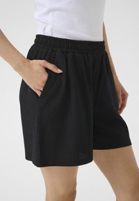Shorts noirs avec une taille élastique, en tissu texturé, poches latérales et coupe décontractée, atteignant le milieu de la cuisse en longueur.