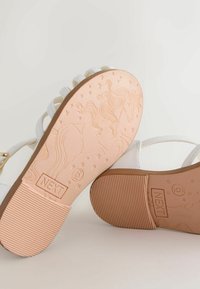 White sandals with a smooth texture and multiple straps. The sole features an embossed unicorn design on a light pink background.