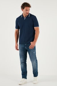 Tamno plavi polo majica s bijelim rubovima na ovratniku i rukavima, uparena s svijetloplavim iskriženim trapericama i bijelim tenisicama.