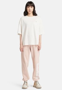 Oversized off-white bomullströja med en liten logotyp, i kombination med rosa sweatpants med vit text "Timberland". Bärs med beiga sneakers.