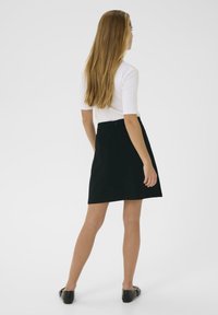 Jupe noire en forme de A en tissu au toucher lisse, avec une fermeture éclair dissimulée au dos et combinée avec un haut blanc ajusté.