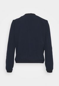 Tmavě modrá bombera bunda s kulatým límcem, dlouhými rukávy a elastickými manžetami. Měkký materiál s hladkou texturou bez viditelných vzorů.