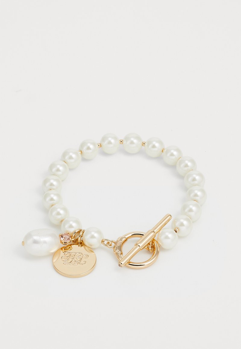 Pulsera de perlas con perlas redondas blancas, cierre de palanca en tono dorado y un charm decorativo con iniciales y un acento rosa.