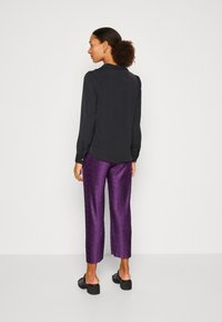 Blusa nera a maniche lunghe con colletto e dettagli con bottoni, abbinata a pantaloni viola testurizzati. Colori solidi, vestibilità rilassata e lunghezza cropped.
