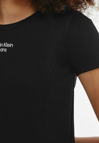 Černé tričko z hladké bavlny s krátkými rukávy. Na horní levé části hrudi se nachází bílé logo "Calvin Klein Jeans".