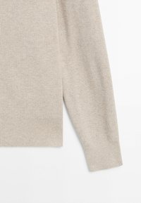 Beiger gestrickter Pulloverärmel und unterer Torso-Bereich mit gerippten Bündchen und Saum auf weißem Hintergrund.