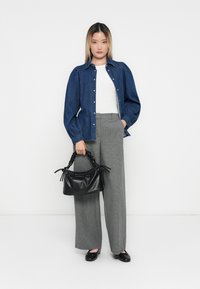 Camisa de ganga com mangas bufantes, top branco ajustado, calças cinzas de perna larga e uma mala preta texturizada com alças trançadas.