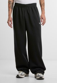 Melnas sporta bikses, kas izgatavotas no mīksta auduma, ar elastīgu jostu un nelielu logotipu. Brīva piegriezuma ar sašaurinātām piedurknēm pie potītēm.