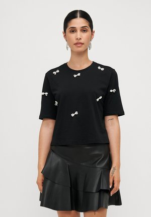 Black cotton t-shirt with short sleeves, featuring small white bow decorations scattered across the front. Paired with a black leather tiered skirt.