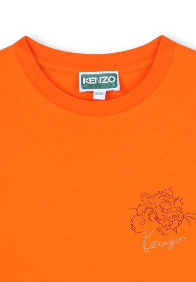 T-shirt en coton orange vif avec un col rond. Présente un graphisme perforé du visage d'un tigre et le nom de la marque "Kenzo" en strass.