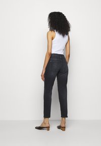 Jeans in denim nero con vita alta, taglio slim e tasche posteriori. Abbinati a un top bianco senza maniche e mules neri con tacco.