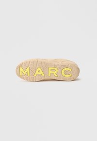 Suela de zapatilla beige con caucho texturizado, presenta una atrevida marca amarilla "MARC" y un patrón de dibujo robusto para mejor agarre.