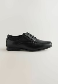 Chaussure formelle noire avec une finition lisse, équipée de lacets et d'un bout légèrement pointu, sur fond clair uni.