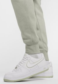 Biele tenisky Nike Air Force 1 so svetlozelenou podrážkou a akcentmi. Majú zaoblenú špičku, hrubé šnúrky a textúrovanú gumenú podrážku.