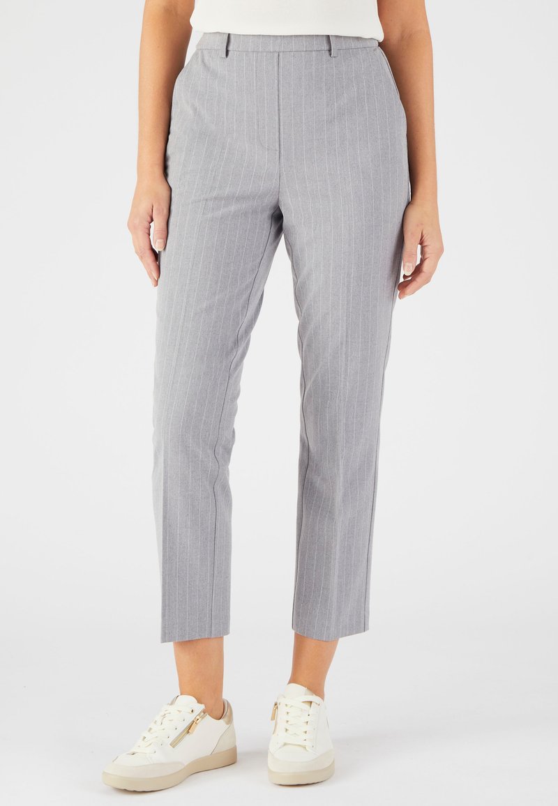 Grijze gepinde broek met een getailleerde pasvorm, cropped lengte en zijzakken, gecombineerd met witte sneakers met gouden ritsaccenten.
