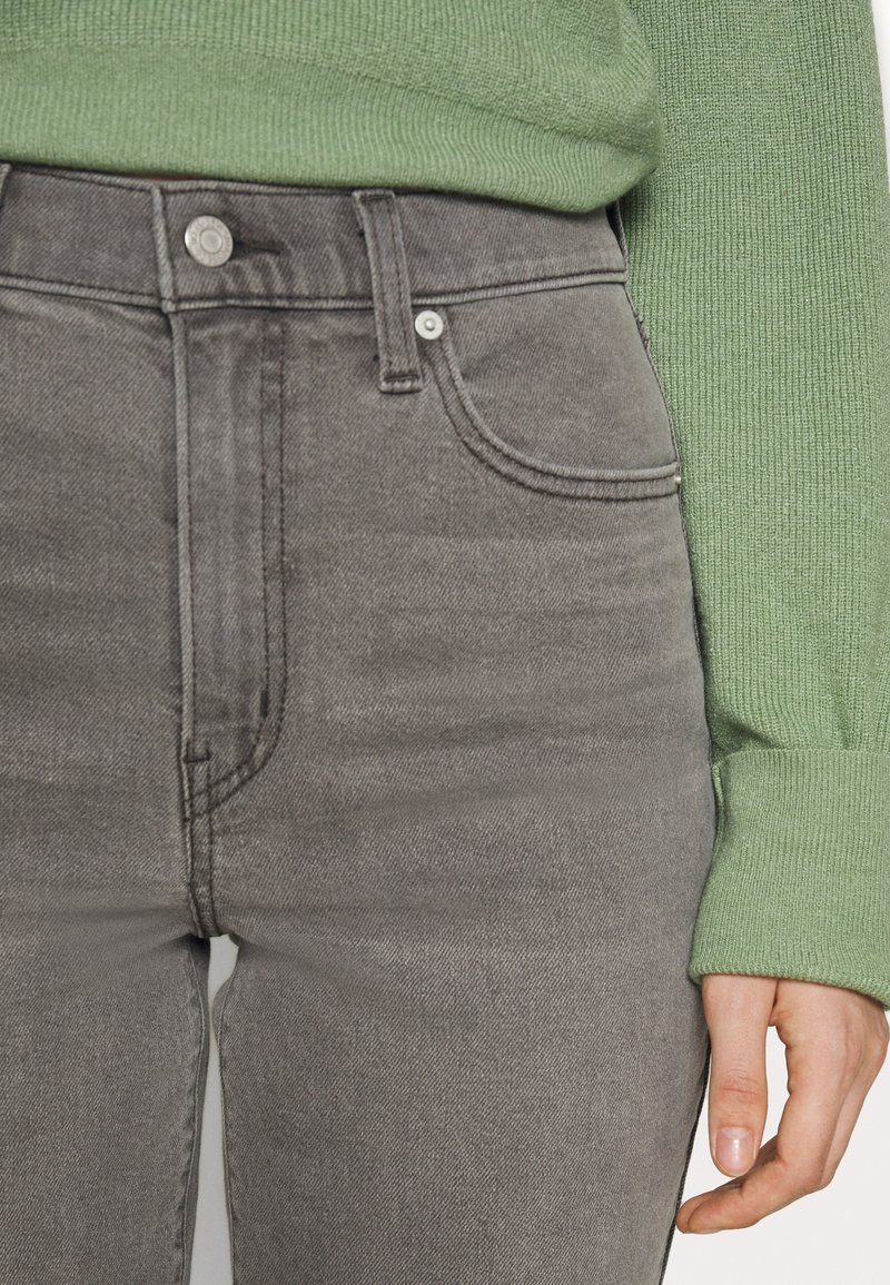 Jeans de mezclilla gris de cintura alta con bolsillos frontales y cierre de botón metálico, combinados con un suéter verde texturizado.