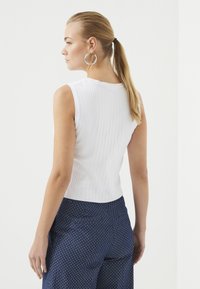 Witte geribbelde mouwloze top met een ronde halslijn, gecombineerd met marineblauwe broek met stippen. Heeft een gladde textuur en een aansluitend ontwerp.