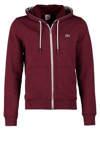 Burgundy zip-up hoodie i bomullsblandning, med dragsko i huvan, framfickor och en liten grön logotyp på vänster bröst.