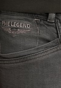 Šedé denimové džínsy s zadnou vreckom s vyšitým logom "PME LEGEND" a dizajnom krídla, doplnené kontrastným prešívaním a hladkou textúrou.