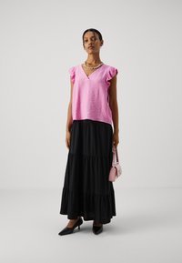 Top rosa senza maniche con maniche a volant, abbinato a una lunga gonna nera a più strati. Accessoriato con una piccola borsa rosa e tacchi neri.