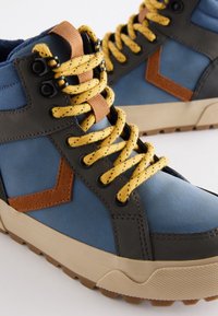 Sneaker alte con tomaia blu, accenti grigi, logo in pelle marrone e lacci gialli. Presentano suole testurizzate e occhielli neri.