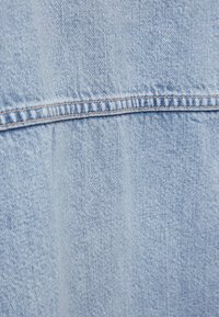 Šviesiai mėlynos spalvos džinsinio audinio su lygiu paviršiumi. Matomi siūlių raštai ir subtilūs spalvų pokyčiai, išryškinantys medžiagos pynimo struktūrą.