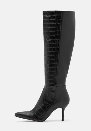 Botte noire hauteur genou à talon aiguilles avec bout pointu, présentant un cuir lisse d'un côté et un cuir à texture crocodile de l'autre.