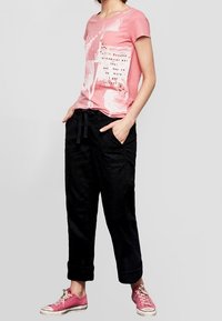 Roze graphic t-shirt met wit ontwerp, gecombineerd met losse zwarte broeken en roze sneakers. Casual fit met opgerolde mouwen en zakken.