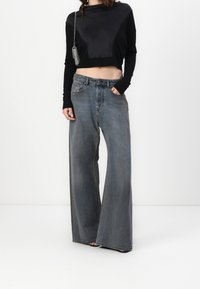 Czarny skrócony top z długimi rękawami i satynowym panelem, zestawiony z wysokimi, szerokimi, wyblakłymi niebieskimi dżinsami. Posiada klasyczny fason z pięcioma kieszeniami.