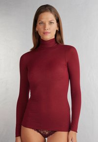 Vinröd långärmad tröja med hög hals i en figurnära design, tillverkad av mjukt, elastiskt tyg med slät yta. Ingen mönstring eller synlig hårdvara.