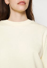 Jasnożółta bluza z prążkowanym okrągłym dekoltem, gładką fakturą i luźnym krojem, charakteryzująca się minimalnym przeszyciem i brakiem widocznych wzorów.