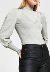 Ljust grå, randig långärmad topp med hög, scalloped halsringning och puffiga axlar, kombinerad med svarta, åtsittande byxor med subtila detaljer.