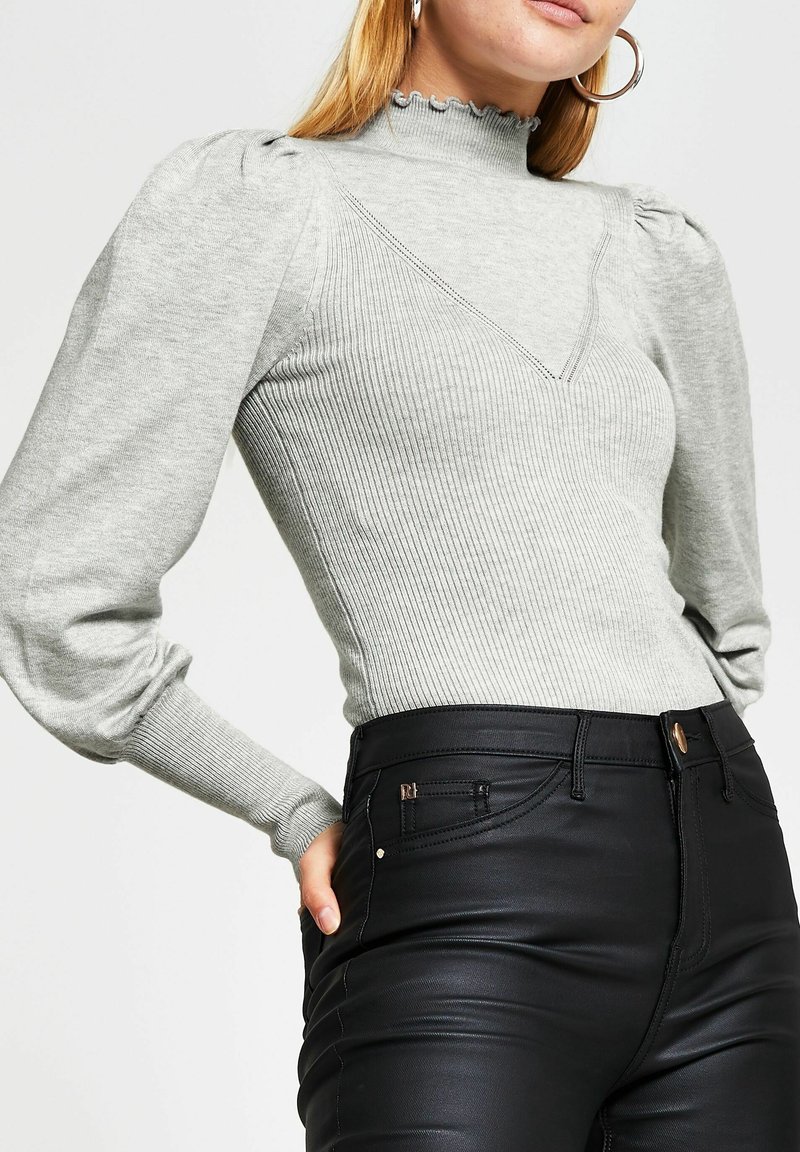 Ljust grå, randig långärmad topp med hög, scalloped halsringning och puffiga axlar, kombinerad med svarta, åtsittande byxor med subtila detaljer.