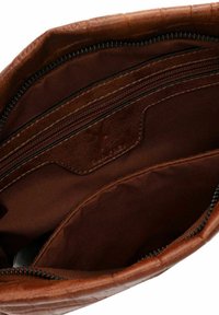 Das Innere der braunen Ledertasche verfügt über zwei Reißverschlussfächer und ist mit einem glatten Stofffutter ausgestattet. Sie hat eine strukturierte Außenseite und ein Markenetikett.