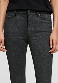 Jeans de mezclilla negros y brillantes con un corte ajustado, que cuentan con un cierre de botón en la parte delantera, pasadores para cinturón y dos bolsillos frontales. Textura suave.